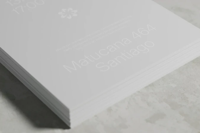 Stack of white paper with light text featuring 'Matucana 464 Santiago' and floral watermark in bright, minimalist, indoor composition.