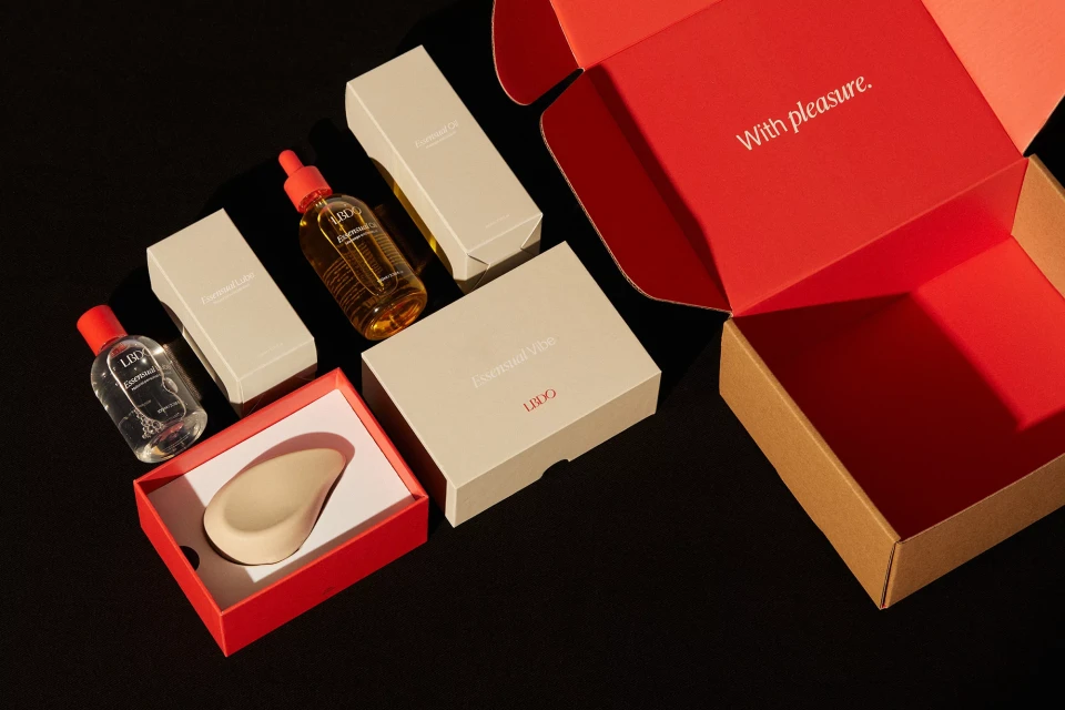 Open box with sex-positive products including lubricant and vibrator, arranged on a dark surface, illuminated by a directional light.