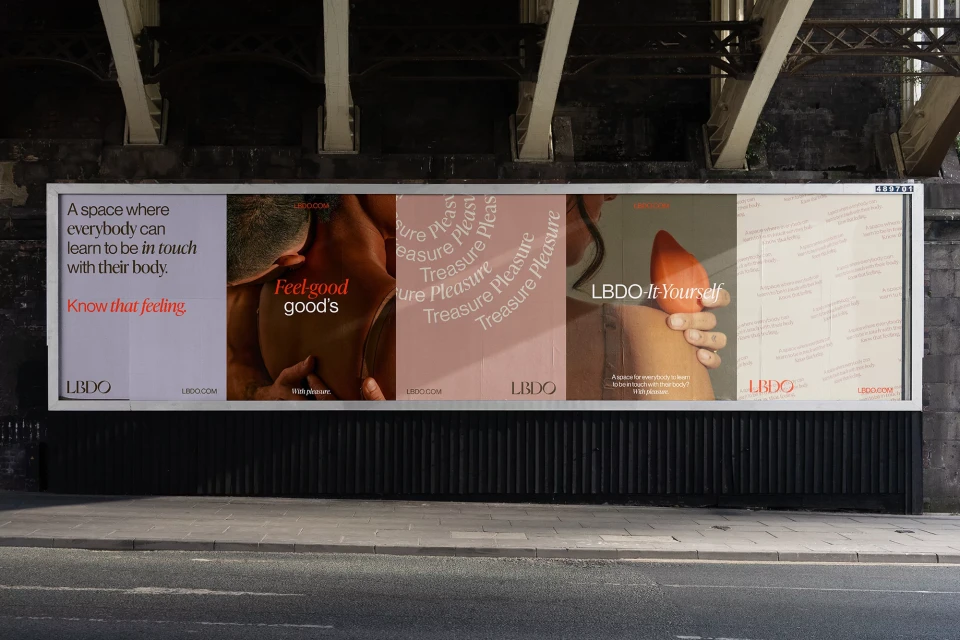 Billboard ad featuring LBDO products and body positivity messaging under a bridge with grey textured ground. Promotes self-discovery.