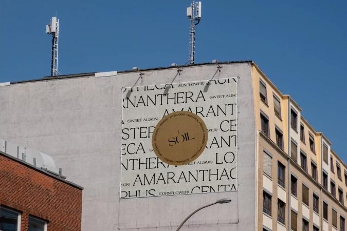 Outdoor advertisement on building wall featuring botanical theme, including a circular emblem, and typography against blue sky.