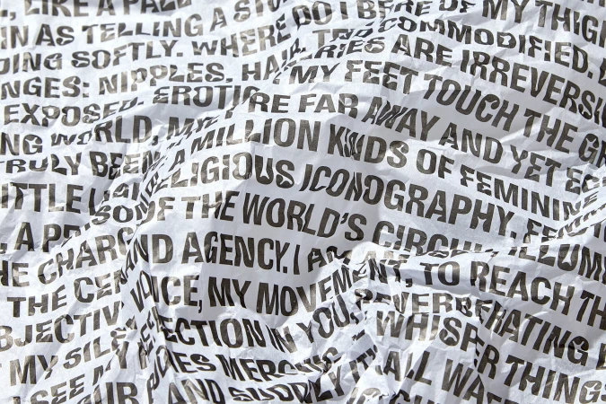 Close-up of crumpled white paper covered in bold black text, creating a textured background with graphic, abstract pattern.