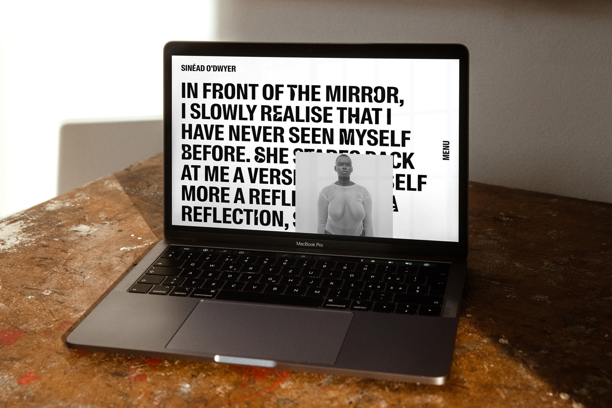 Open laptop displaying a website featuring a black and white portrait of a woman and large, bold text on a rustic wooden surface.