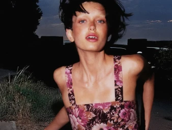 Portrait of a woman with short dark hair wearing a pink floral print dress outdoors at dusk.