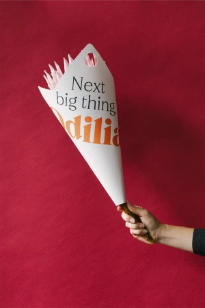Hand holding a white paper bouquet wrapper printed with Odilia branding against a textured red background