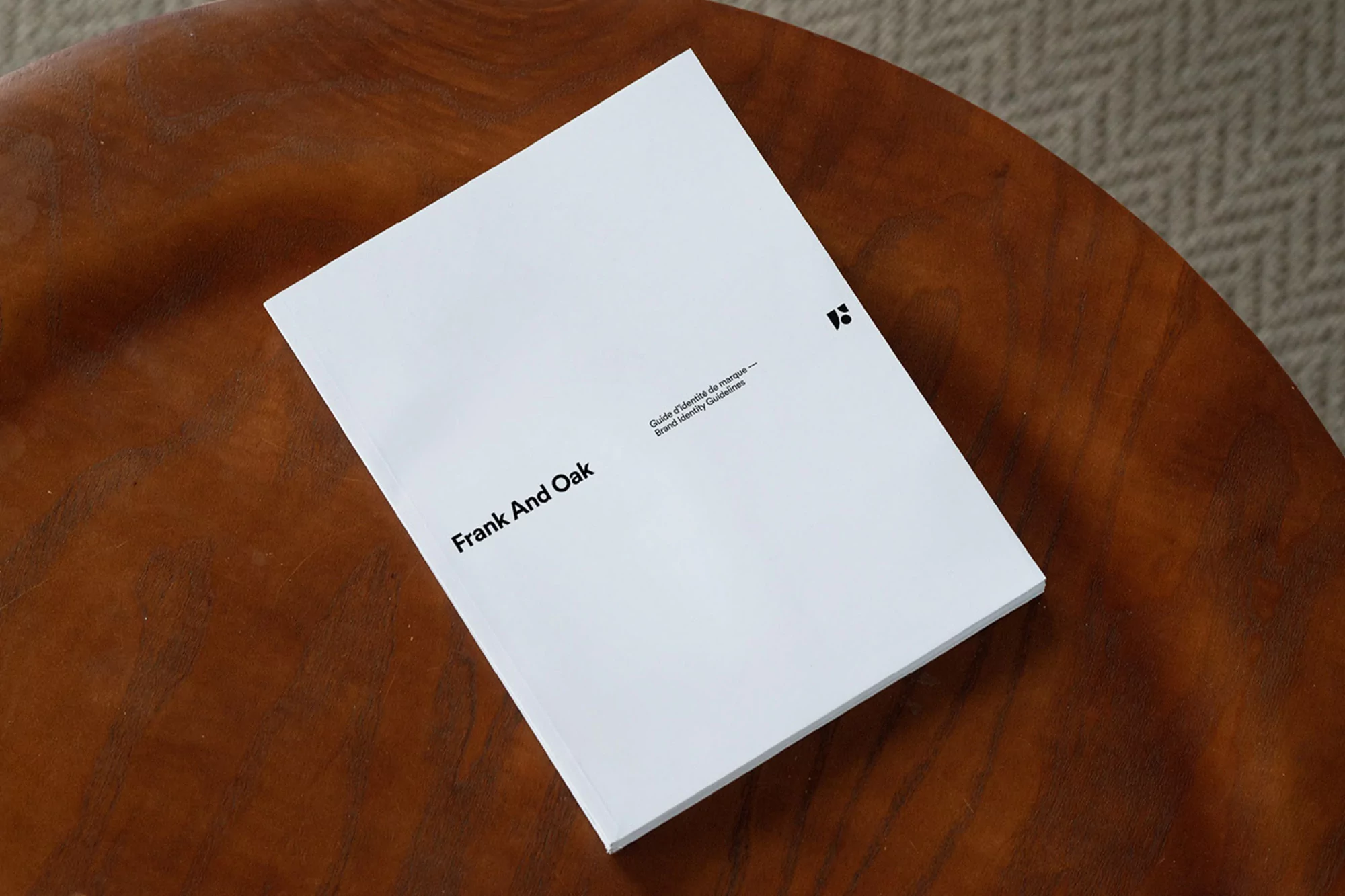 Frank and Oak brand identity guidelines book on a wooden table. The book is white with black text and a logo. Interior shot.