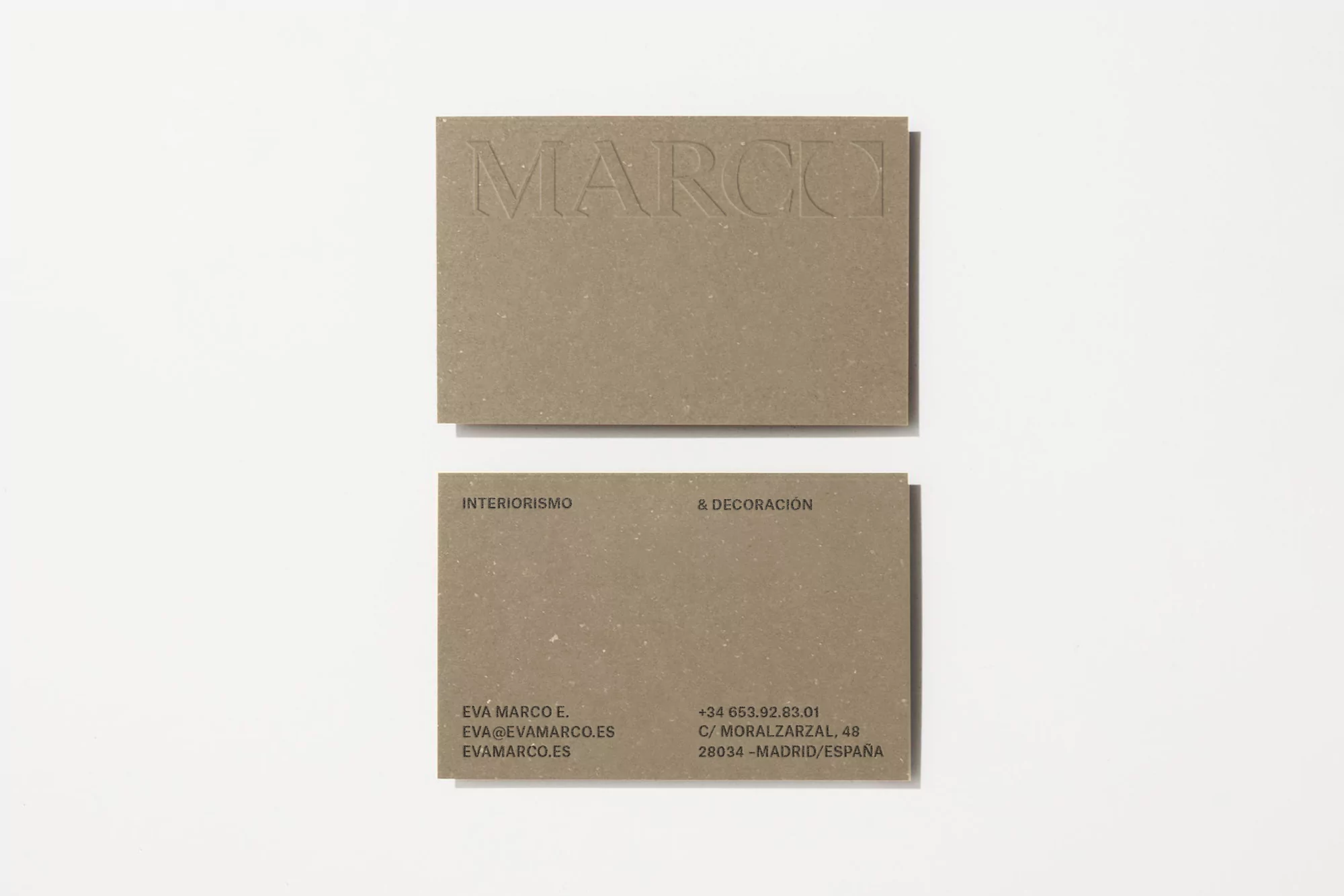 Two textured beige business cards with embossed text sit on a white surface, the top card displaying the company name 'MARCO'.