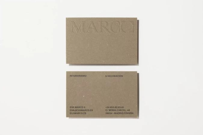 Two textured beige business cards with embossed text sit on a white surface, the top card displaying the company name 'MARCO'.