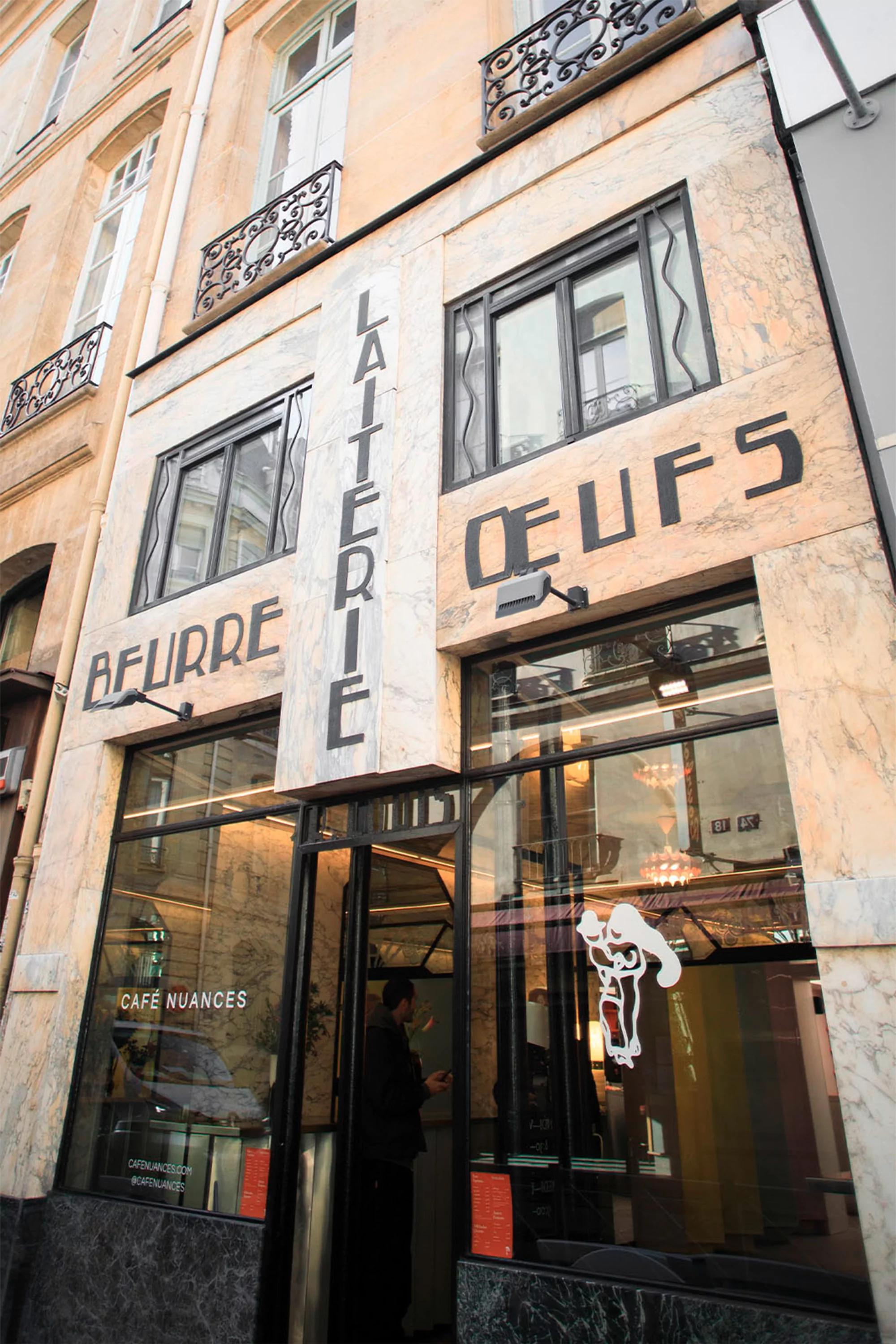 Cafe facade with marble exterior and dark window frames, featuring prominent black lettering, including the words 'Laiterie' and 'Oeufs'.