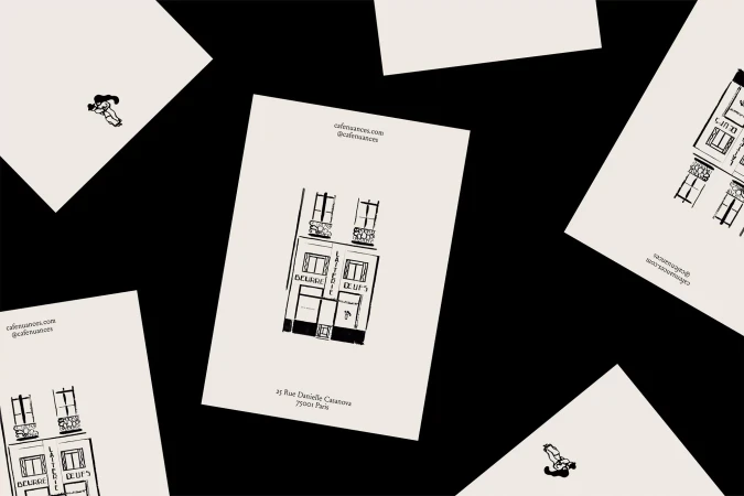Illustration of a building facade on scattered cards against a black background, featuring cafe details and a small figure.