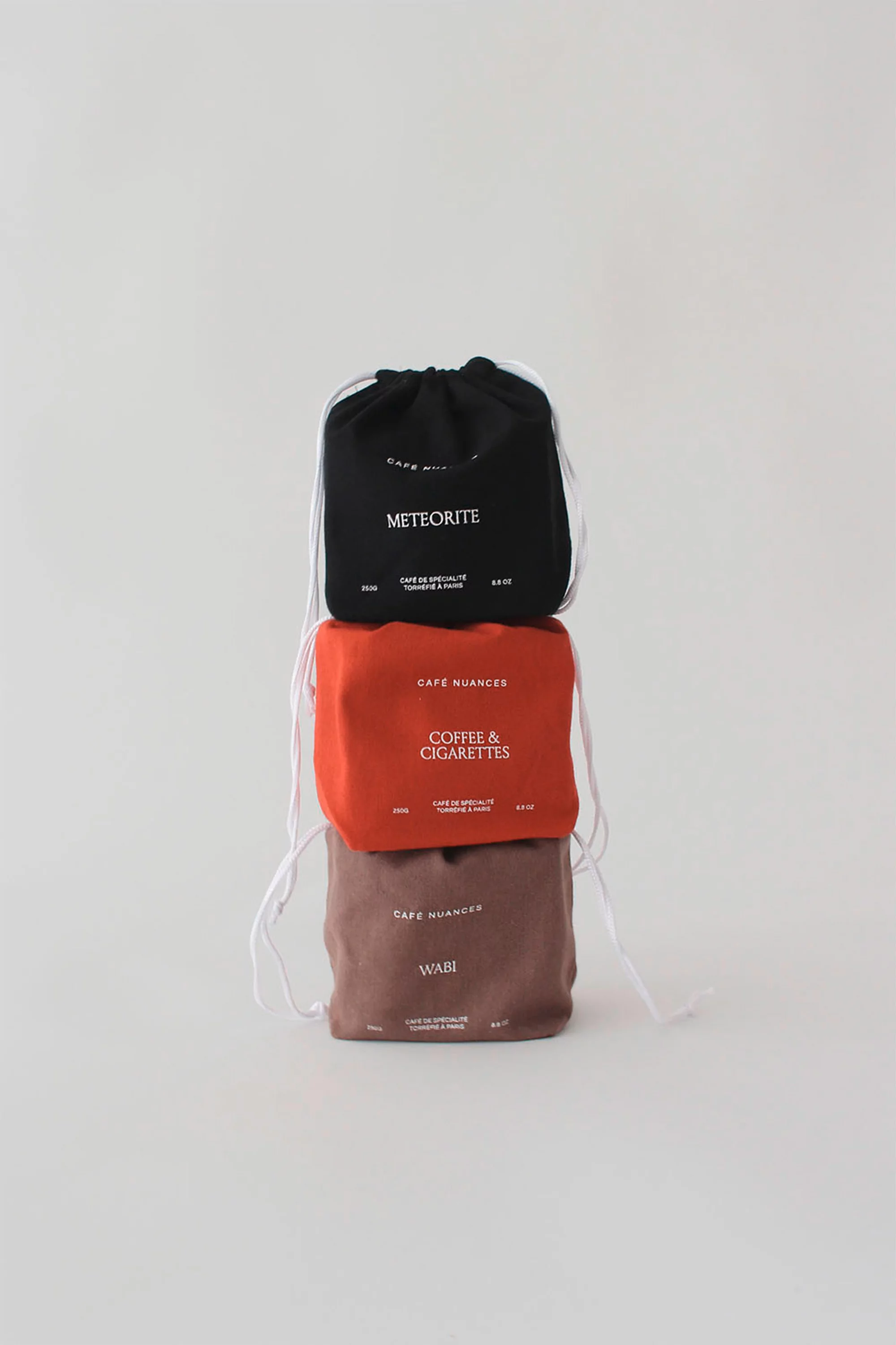 Stack of three small drawstring gift bags in black, rust, and brown tones with white printed text against a plain white background.