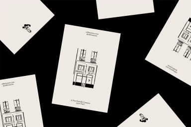 Scattered cream paper cards featuring black ink illustrations of a Parisian storefront against a solid black background.