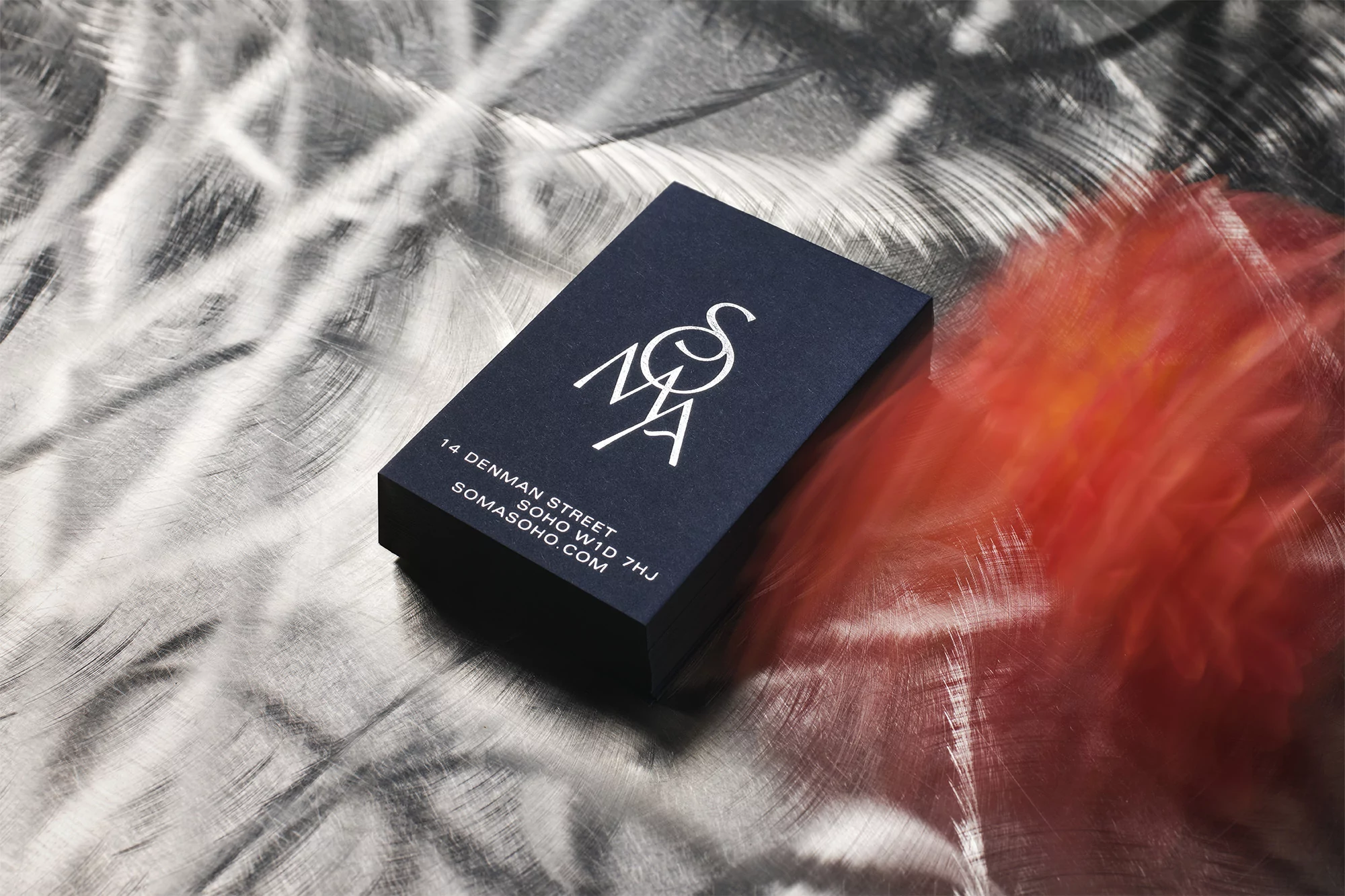 A dark blue business card with white text sits diagonally on a silver metallic background with a diffused orange light reflection.