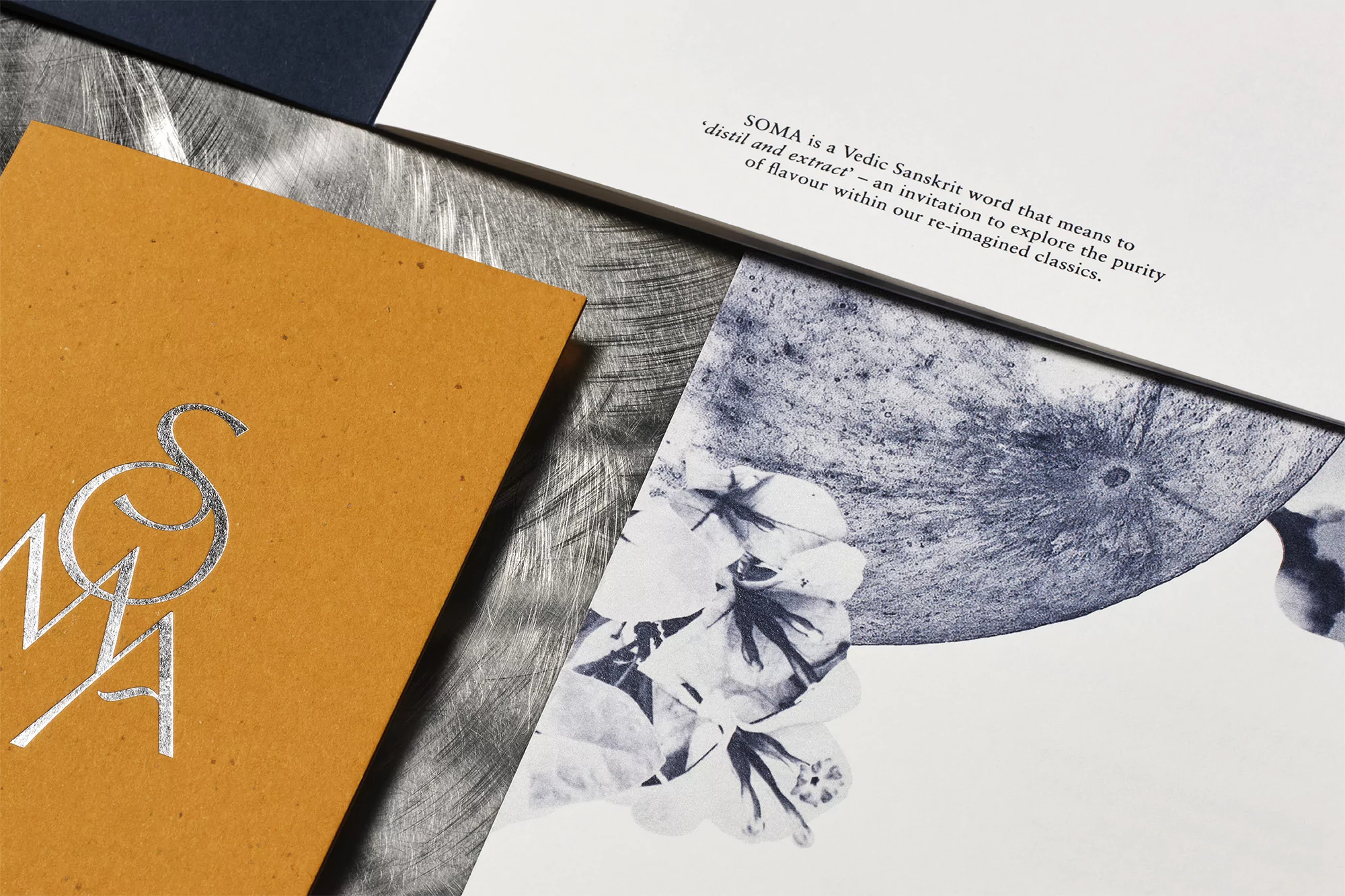 Close-up of stationery featuring an artistic floral design and text, including 'SOMA,' against a textured metallic background.