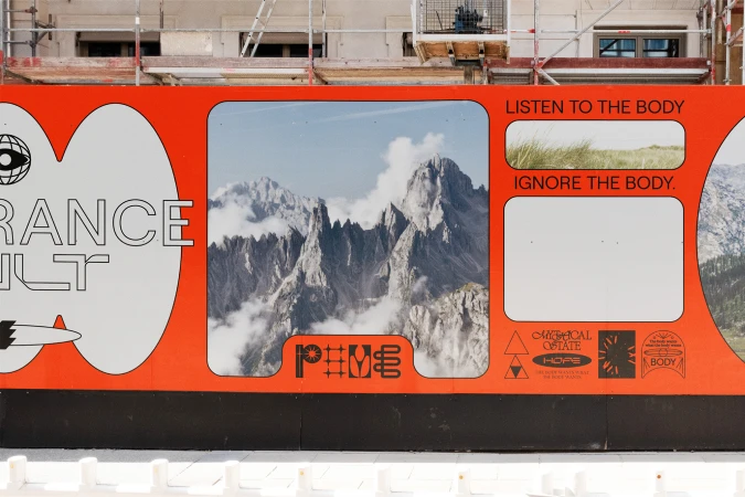Outdoor hoarding featuring mountain range, grass, and text art with an orange background, promoting themes of body awareness and hope.