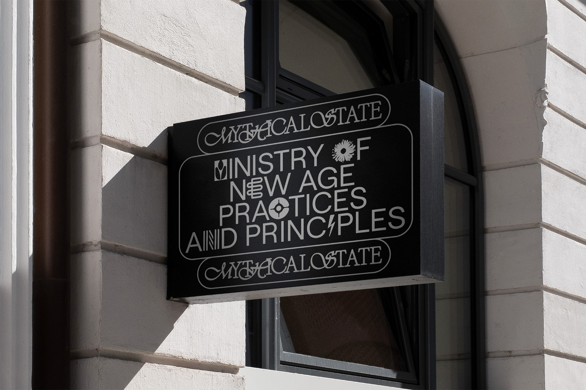 Exterior shot of a black sign for 'Ministry of New Age Practices and Principles' on a white stone building next to a window.