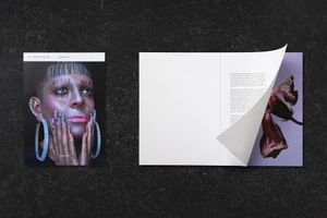 An open magazine layout by Arctic Paper featuring a close-up portrait with text tattoos and an interior page with text and floral image.