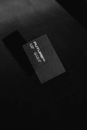 Close-up of a black business card on a textured dark surface. The card features minimal white text with company and contact details.