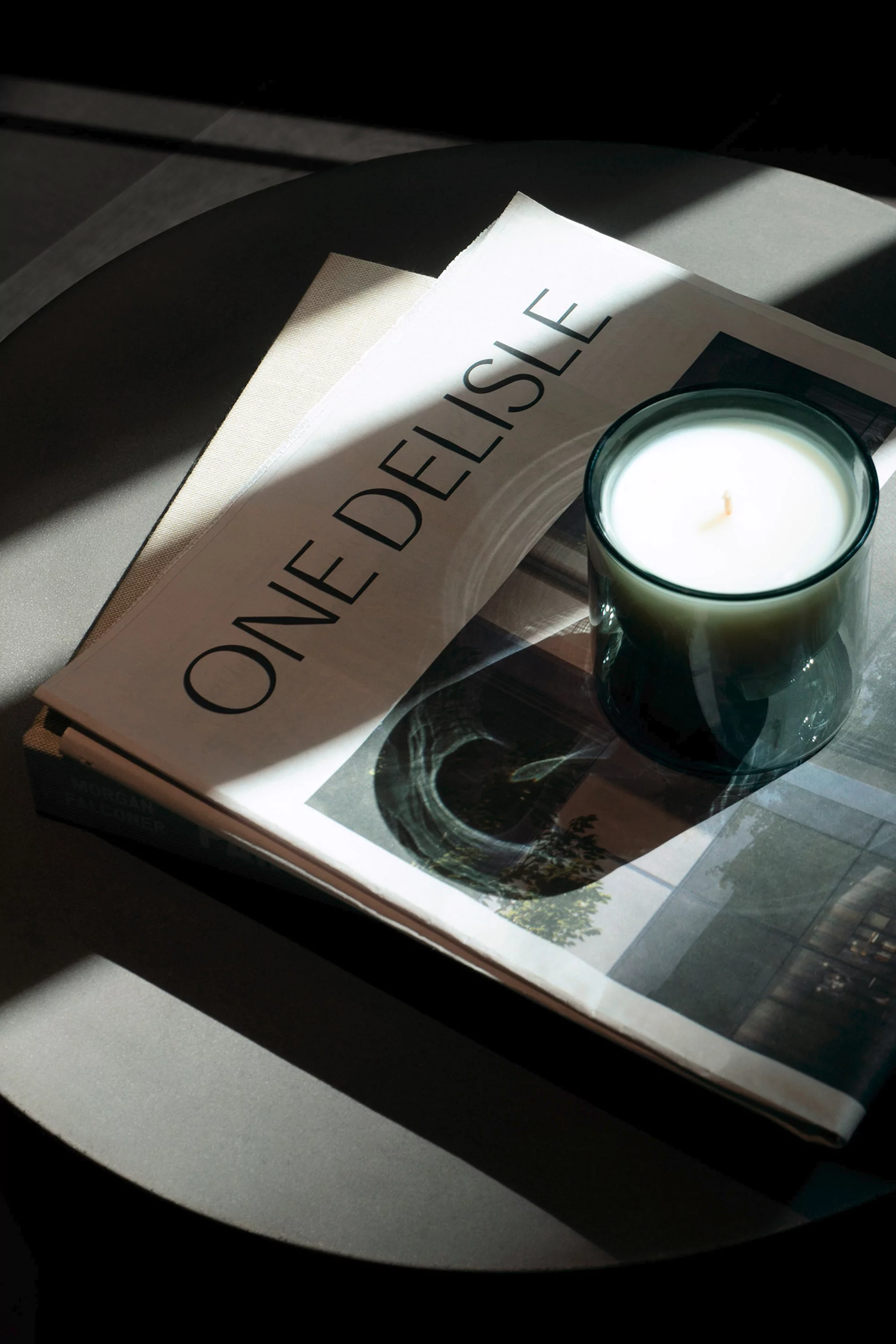 Still life of a lit candle on a newspaper placed on a round table in a shadowy setting with a soft lighting effect.