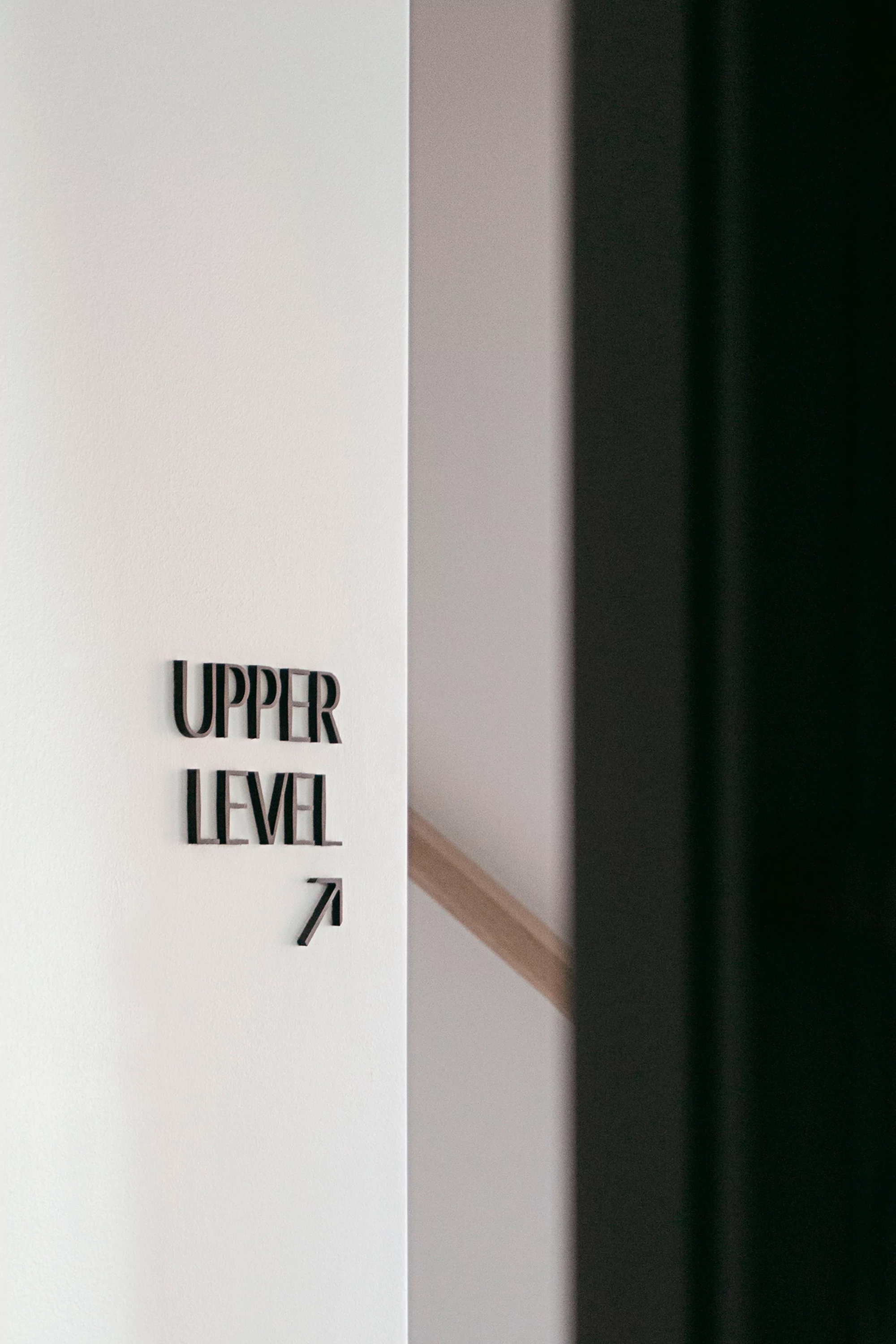 Indoor shot of a white wall with black lettering indicating 'Upper Level 7' along with an arrow, next to a dark, blurred object.