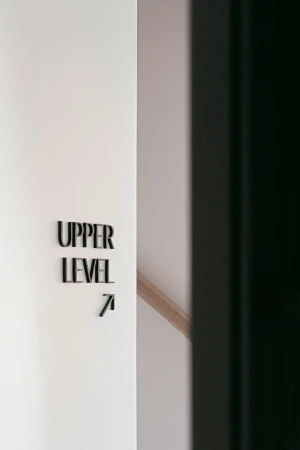Indoor shot of a white wall with black lettering indicating 'Upper Level 7' along with an arrow, next to a dark, blurred object.