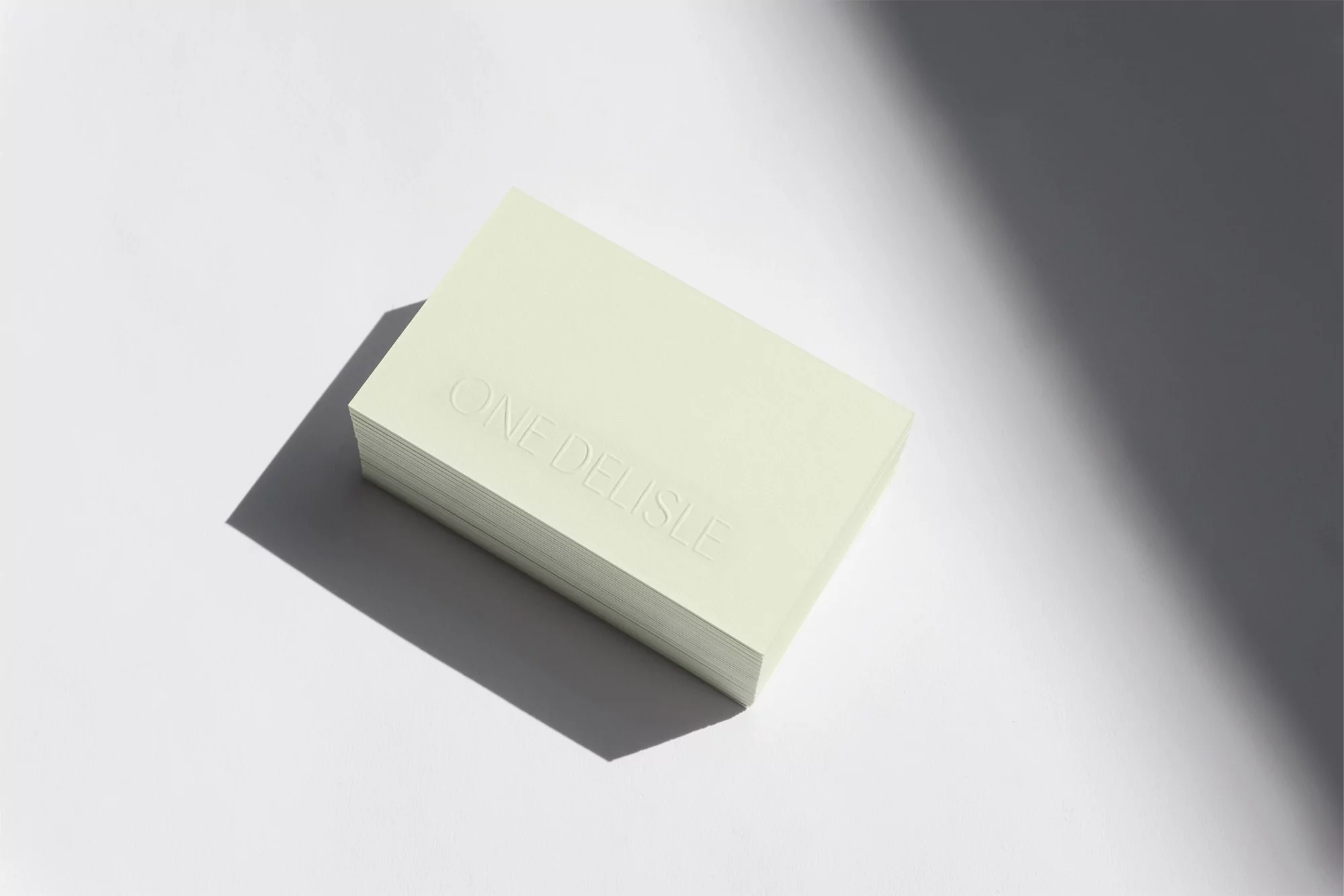 A stack of light yellow business cards sits on a white surface in soft light with the embossed text 'ONE DELISLE' visible.
