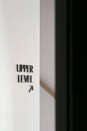 Black dimensional lettering spelling UPPER LEVEL with an upward arrow on a clean white architectural wall next to a dark frame