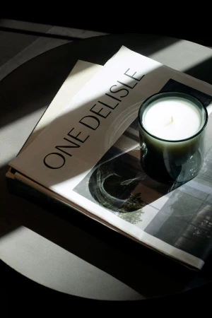 Close-up of a branded publication reading One Delisle and a lit candle in a glass container on a dark round table.