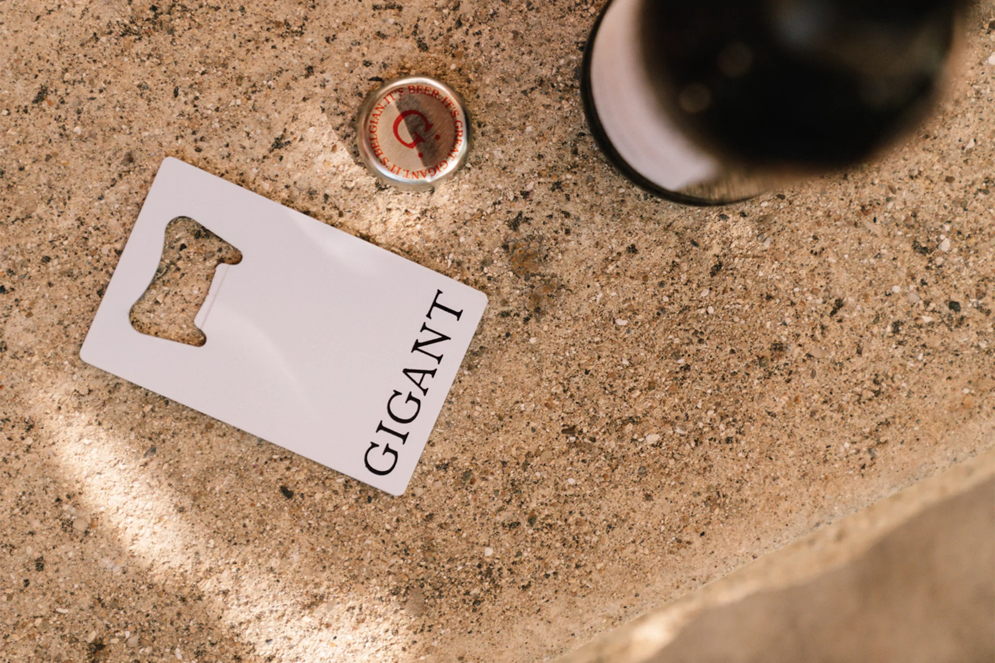 Overhead shot of a bottle opener, bottle cap, and a partial bottle on a textured surface in a close-up still life composition.