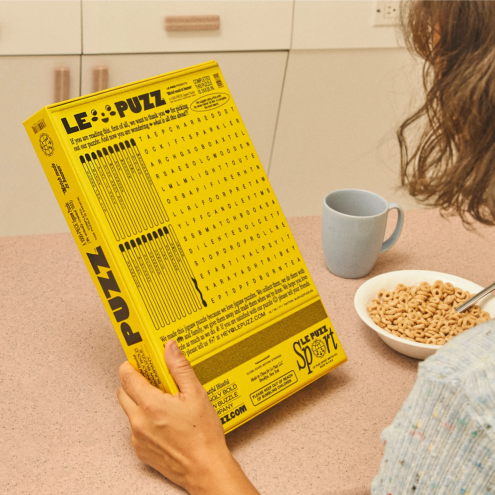 Close-up of a Le Puzz sport puzzle held by a person in a kitchen with a bowl of cereal and mug on a pink counter.