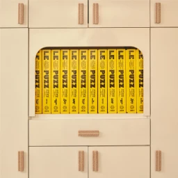 A row of yellow Le Puzz brand puzzle boxes lined up inside an arched cabinet niche with cream cabinetry.