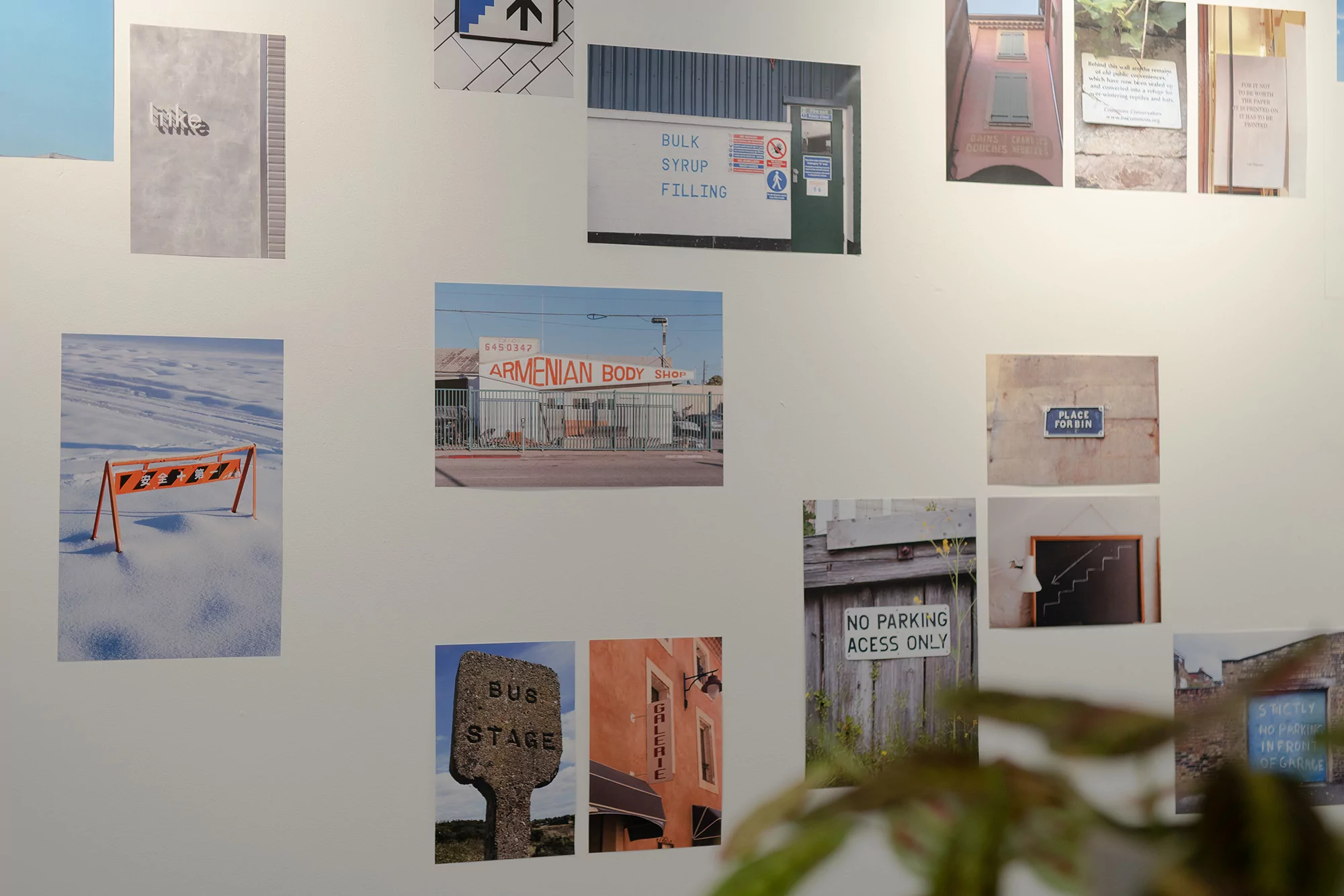 Display of photographs and signs mounted on a white wall, including images of snow, buildings, and various signage.