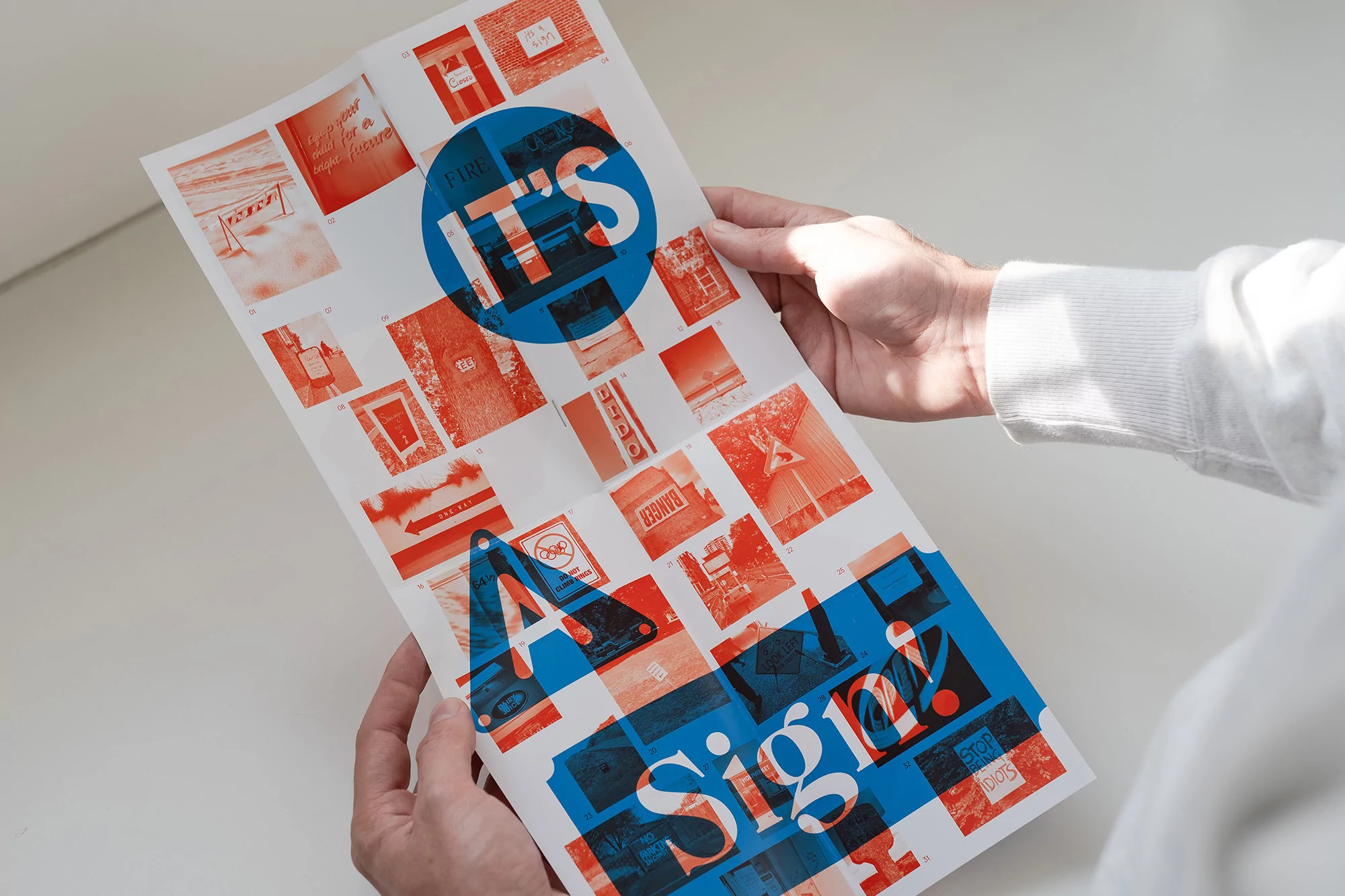 Hands holding a poster featuring a collage of red and blue images, signs, and text, presented against a plain background with soft lighting.