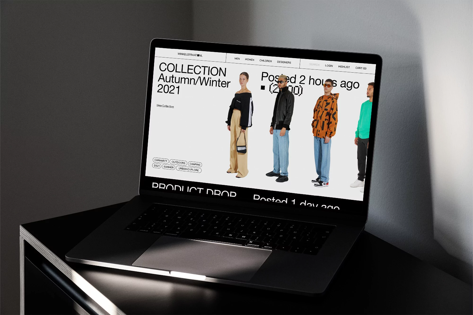 Laptop on a table displays a website with fashion models, Autumn/Winter 2021 collection. The clothing and digital display are the primary focus.