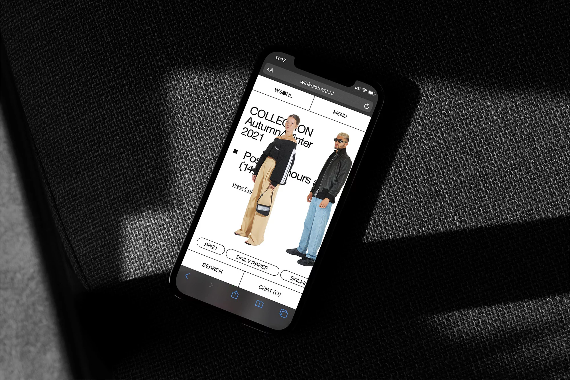 Fashion collection by WSNL showcased on a smartphone display, featuring two models wearing stylish outfits against a dark fabric background.