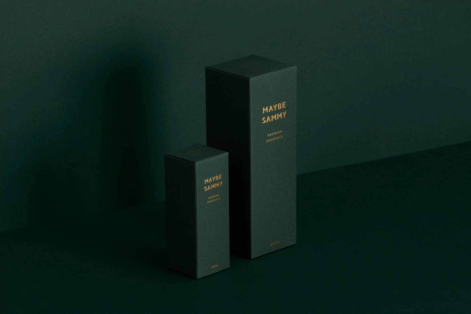Two dark green rectangular boxes of different sizes with gold text 'Maybe Sammy Premium Cocktails' are against a dark green backdrop.