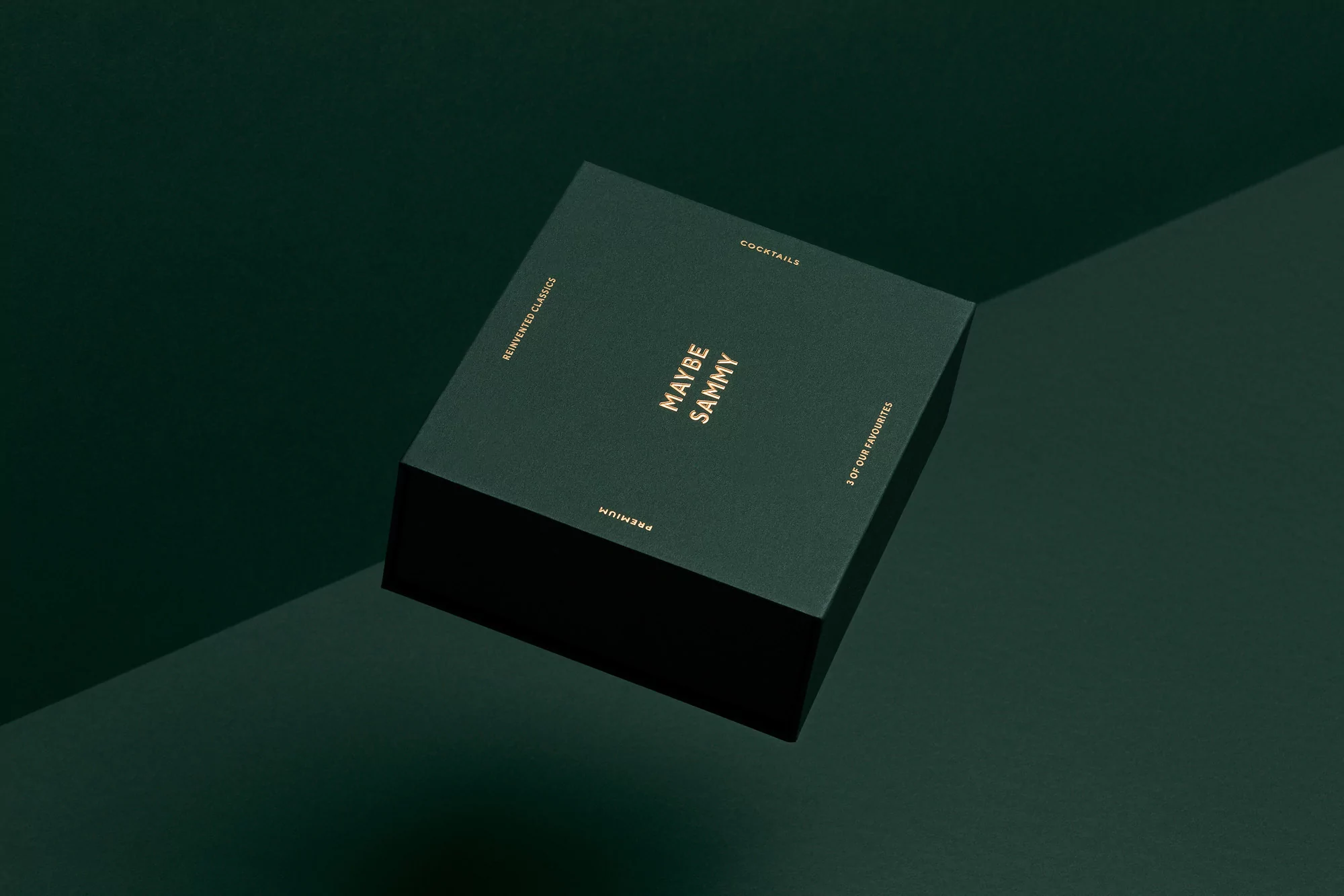 Angled view of a square, dark green 'Maybe Sammy' cocktail box with gold lettering against a matching two-tone green background.