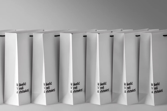 Row of identical white shopping bags with black handles, arranged in a repeating pattern against a gradient gray background, studio lighting.