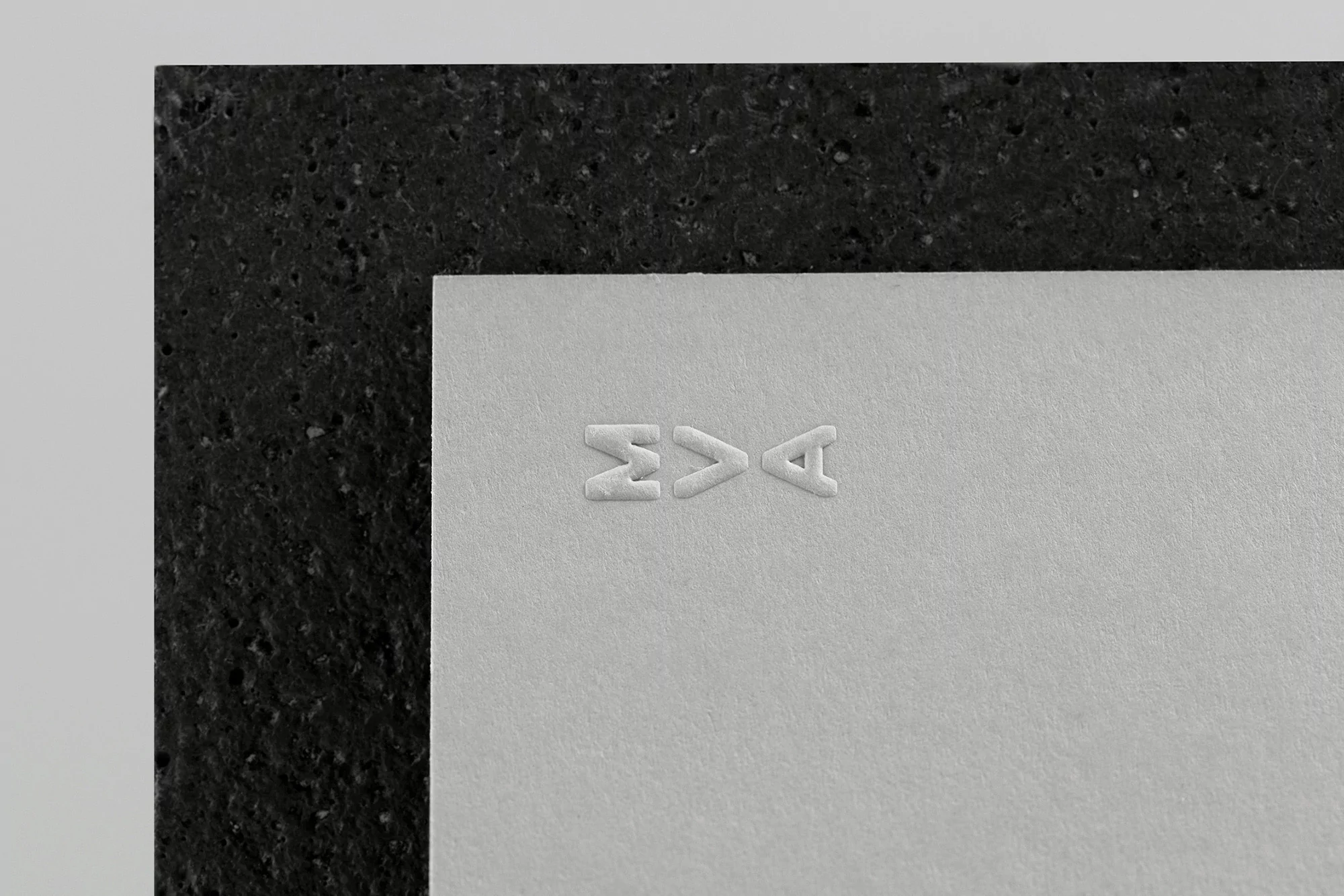 Close-up of white cardstock with embossed text, partially layered on a textured black stone slab against a light gray surface.