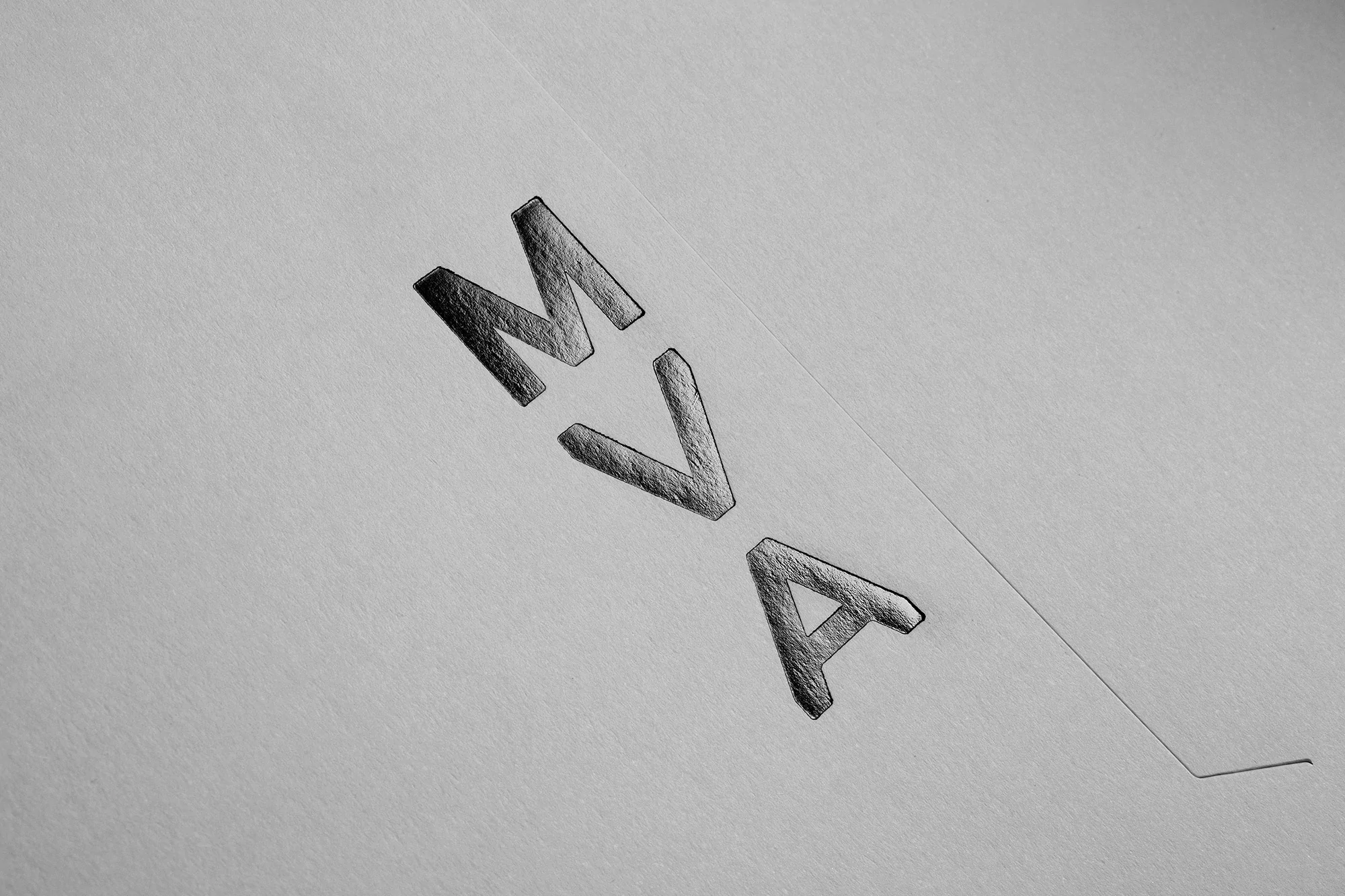 Monochromatic close-up of the letters MVA, engraved or embossed in a white textured surface, capturing simplicity and subtle textural detail.