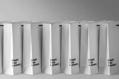 A line of white paper shopping bags featuring branded black typography against a seamless light grey background.