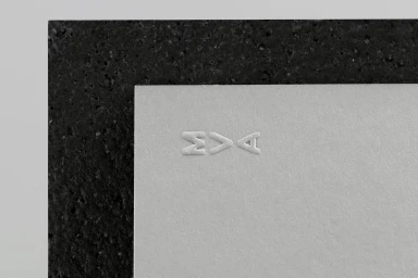 Close-up macro shot of MVA debossed logo on light grey textured paper framed by a dark porous border