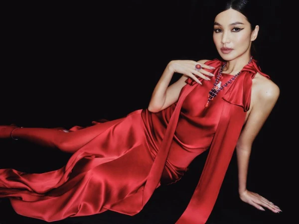 A woman in a red satin gown and red jewelry is reclining against a black background in an indoor fashion or celebrity portrait.