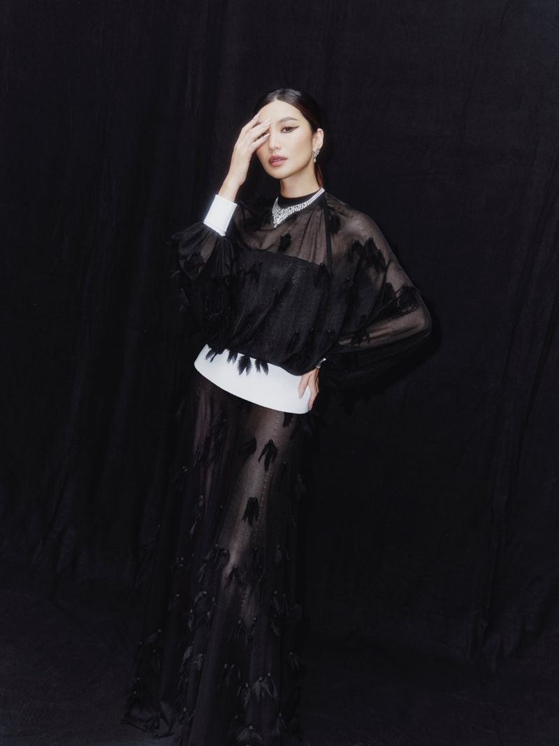 Elegant portrait of an Asian woman in a sheer black gown, set against a dark backdrop, highlighted by soft lighting.