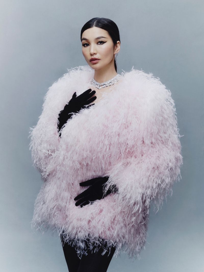 Portrait of Asian woman with feather coat and diamond necklace against light blue background in a studio fashion shot.