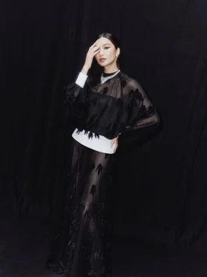 Gemma Chan in a black sheer outfit with white accents against a dark backdrop for Vogue Singapore editorial