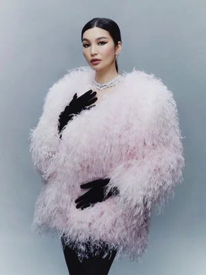 Gemma Chan wearing a fluffy pink feather coat and black gloves against a grey studio backdrop