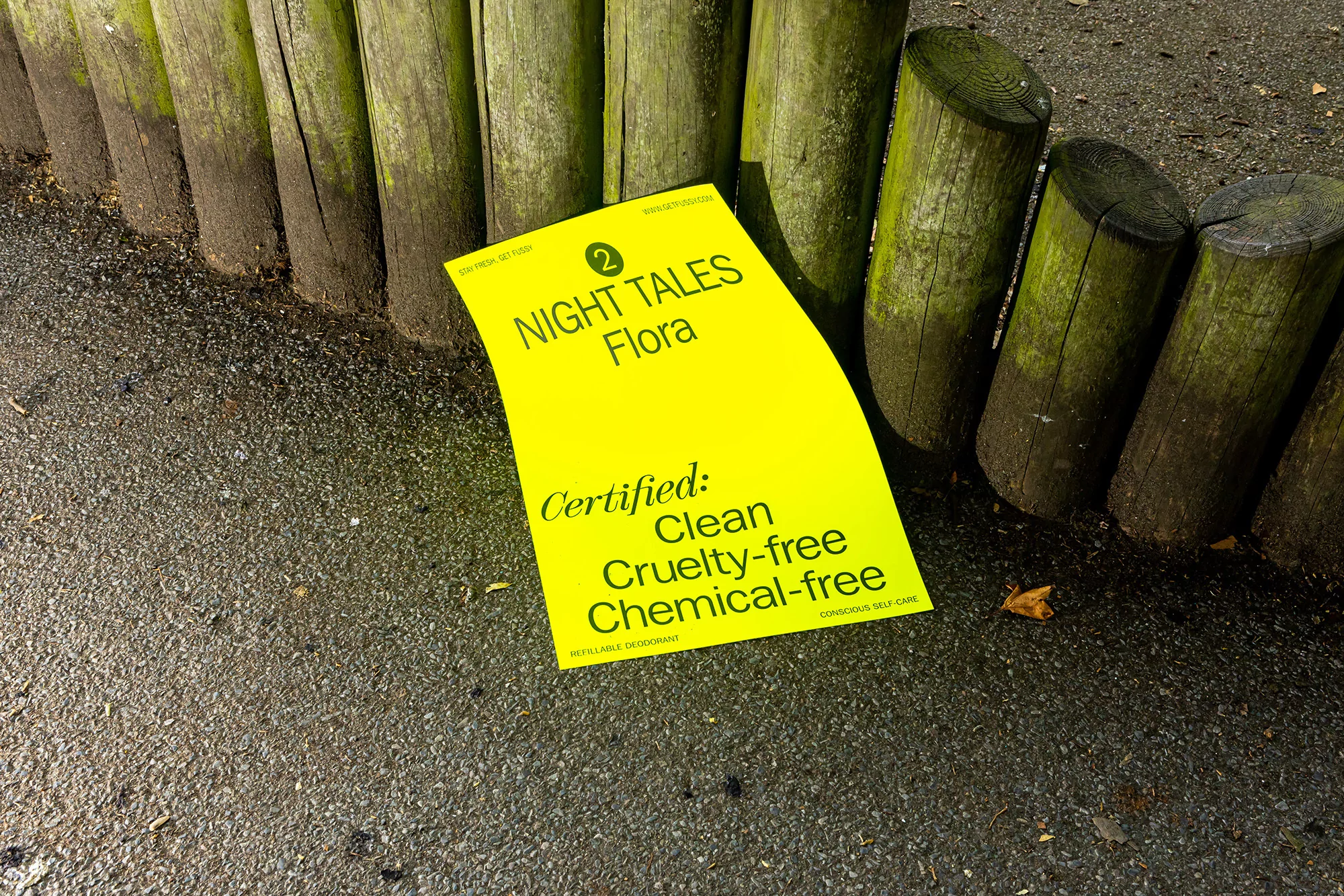 Bright yellow sign on the ground near wooden posts; text reads 'Night Tales Flora,' 'Certified Clean Cruelty-free Chemical-free'.