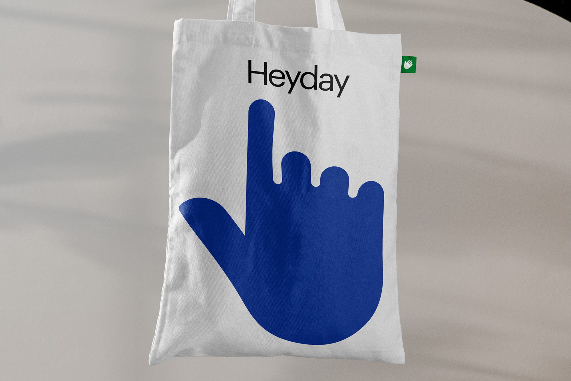 White tote bag with blue hand graphic and the text 'Heyday' in black. Minimalist studio shot against a neutral background.