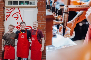 Three men wearing red aprons stand smiling outside a red brick building with a painted white door under natural light.