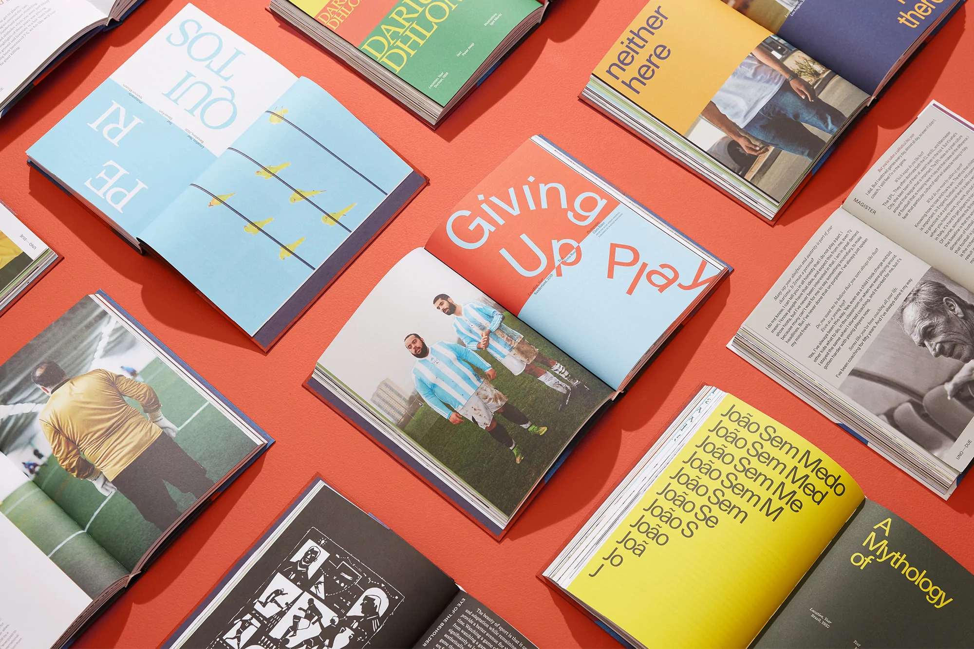 Several open books with colorful graphic design and photography are arranged on a red background, creating a visually engaging composition.